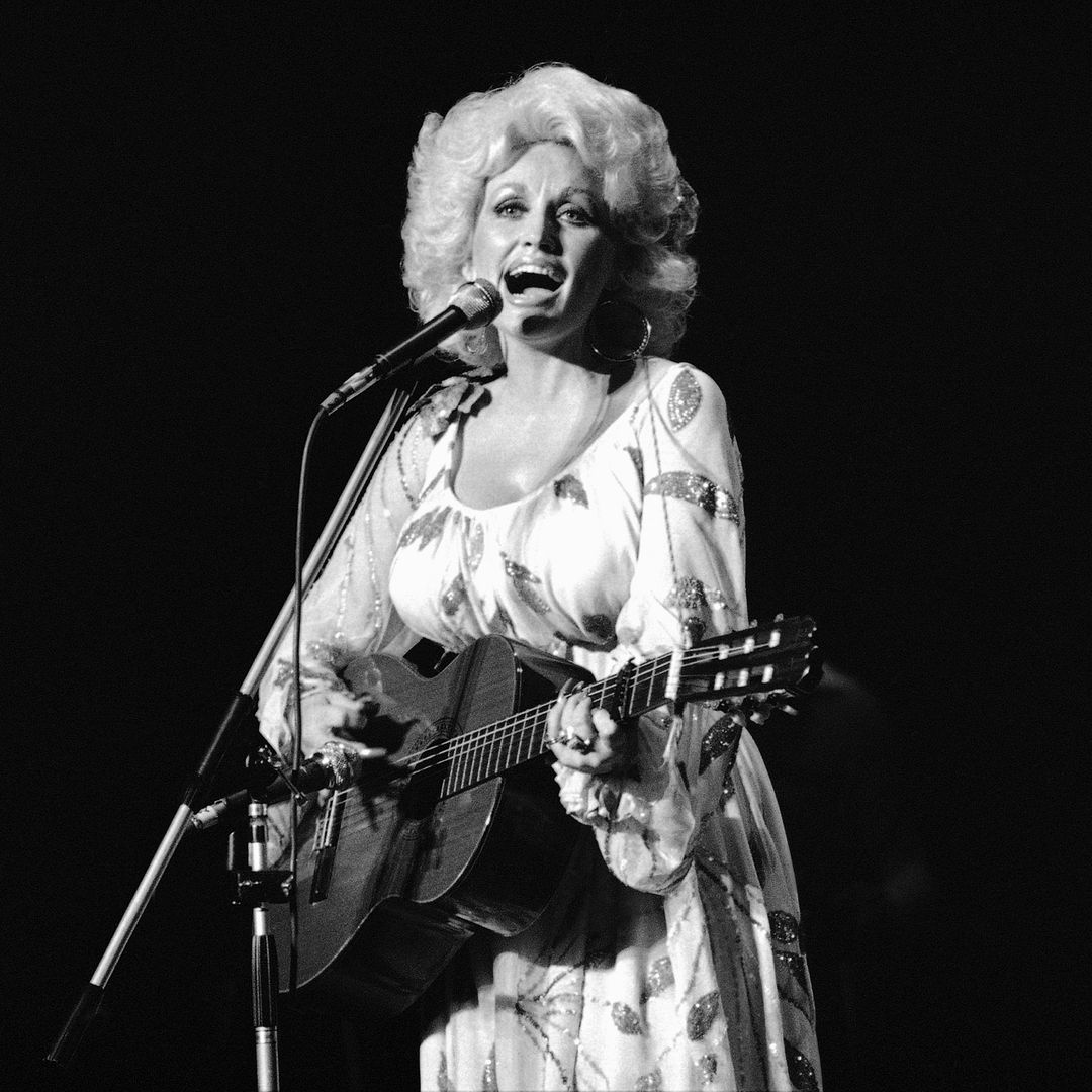 Dolly Parton cantando frente a micrófono y tocando la guitarra