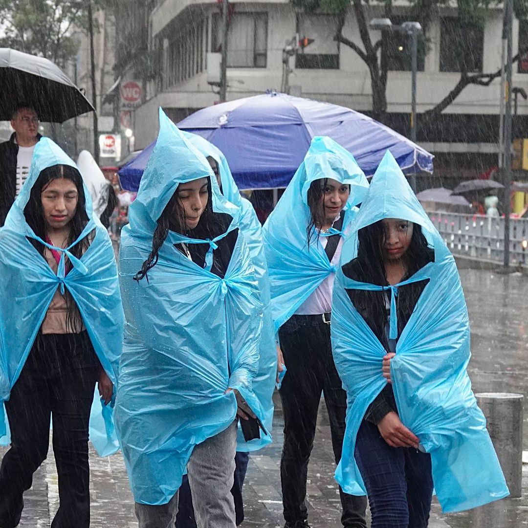 Grupo de personas se cubre con impermeables azules ante fuertes lluvias en la Alameda Central, CDMX, en junio 2026. Foto: Cuartoscuro