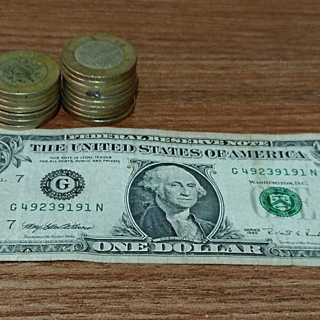 Monedas de 10 pesos mexicanos y un billete de un dólar estadounidense