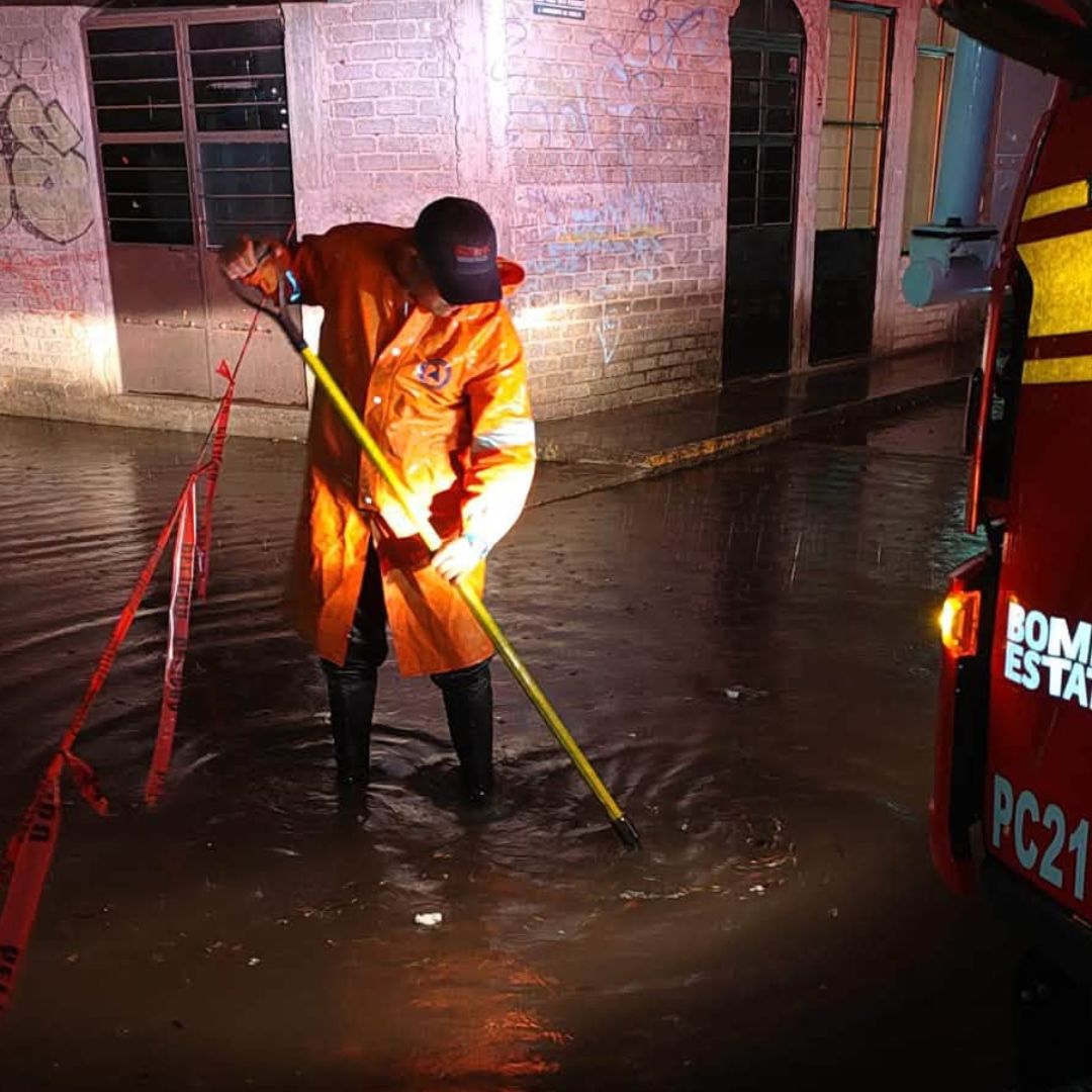 Un elemento de Protección Civil de Michoacán intenta destapar una coladera tras una inundación