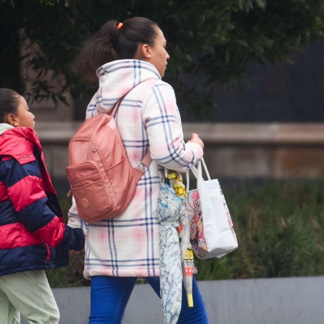 Una madre y su hija caminan abrigadas para protegerse de una tarde lluviosa en Toluca