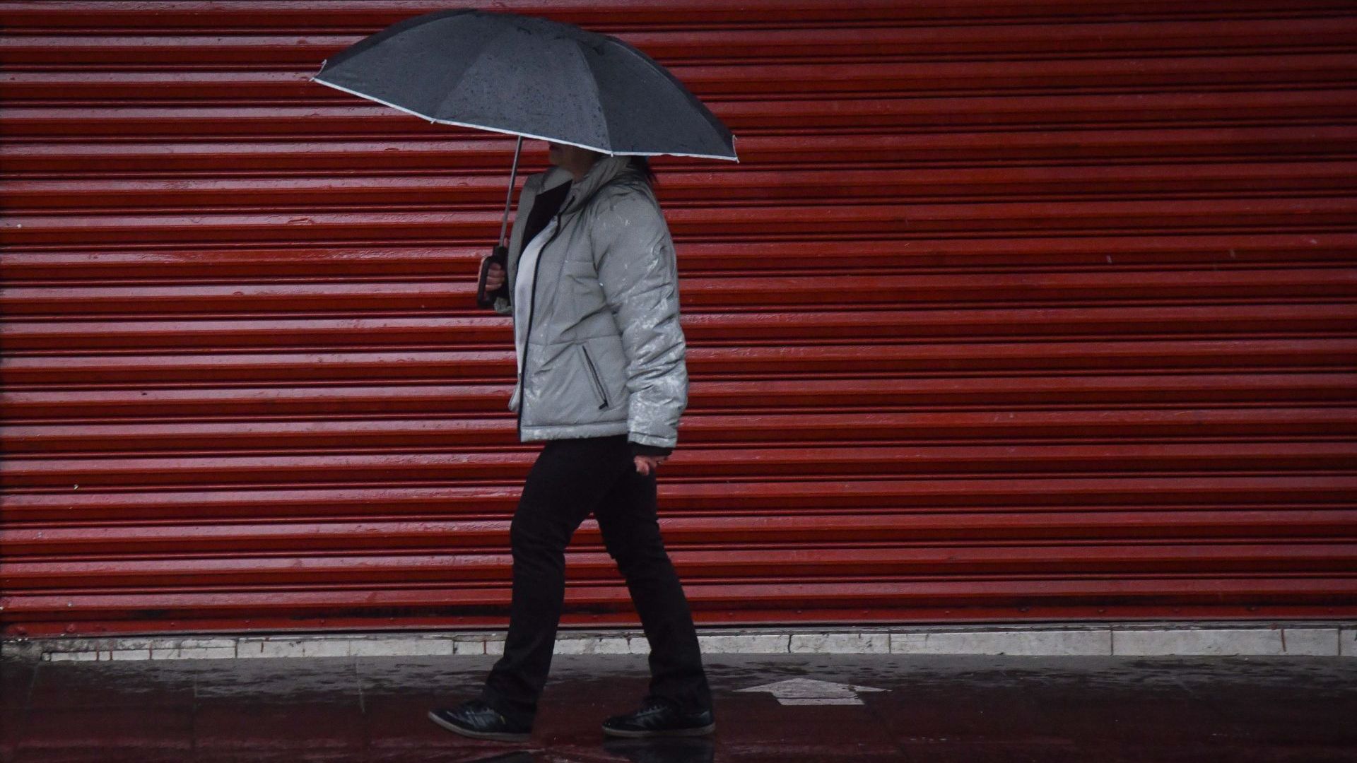 Un bombre camina protegiéndose de la lluvia con una sombrilla
