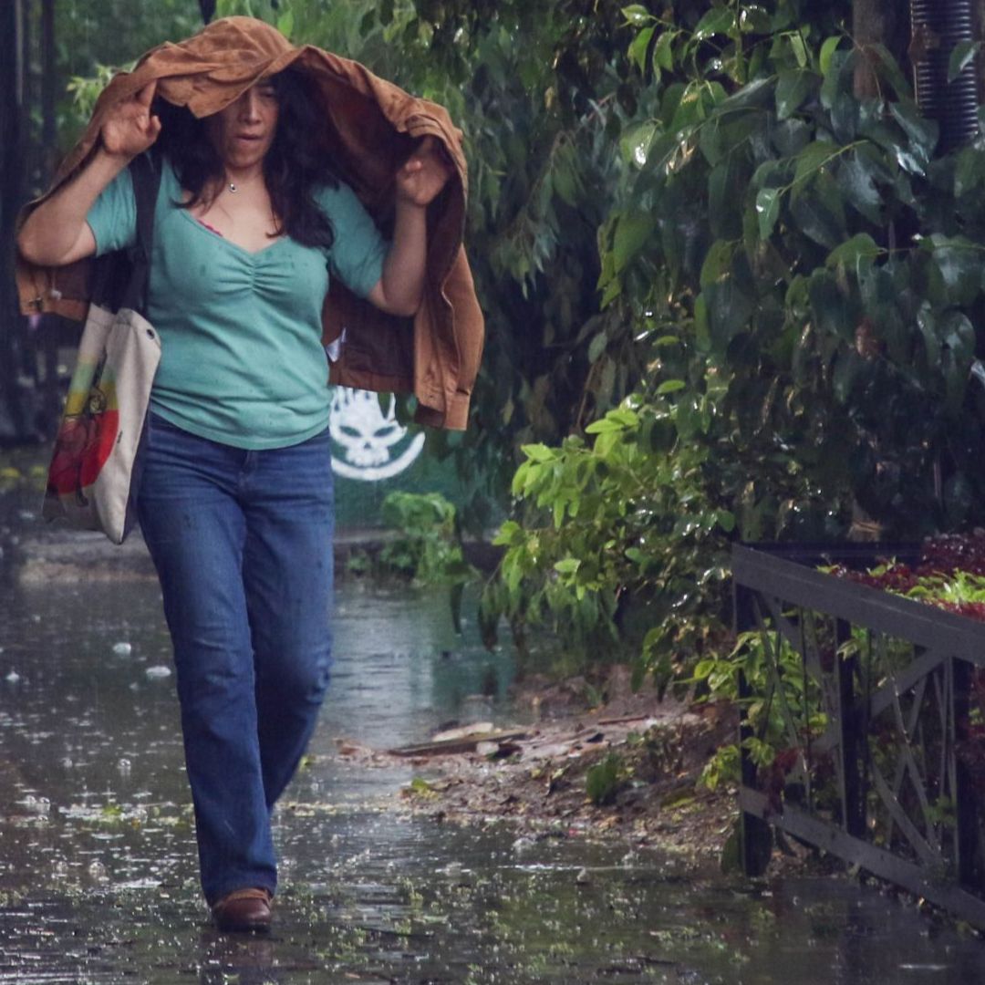 Una mujer se cubre con su abrigo de una lluvia en la Ciudad de México