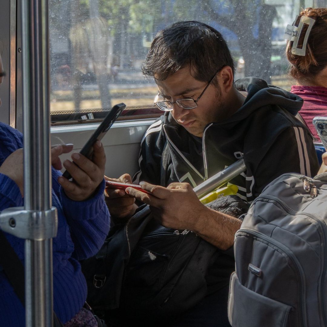Personas viajando en el transporte público usan sus celulares.