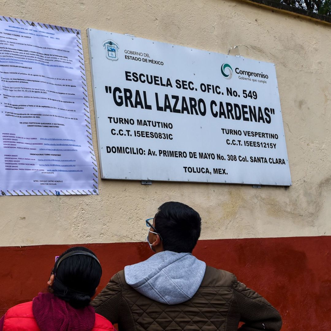 Dos personas revisan indicaciones afuera de una escuela, que incluye la Carta de Asignación de la SEP